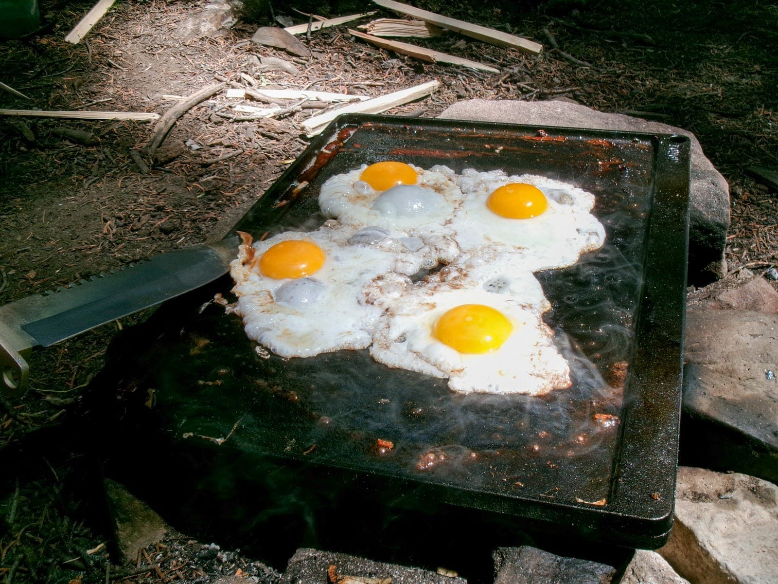 Fried eggs cooking on a well-seasoned outdoor griddle