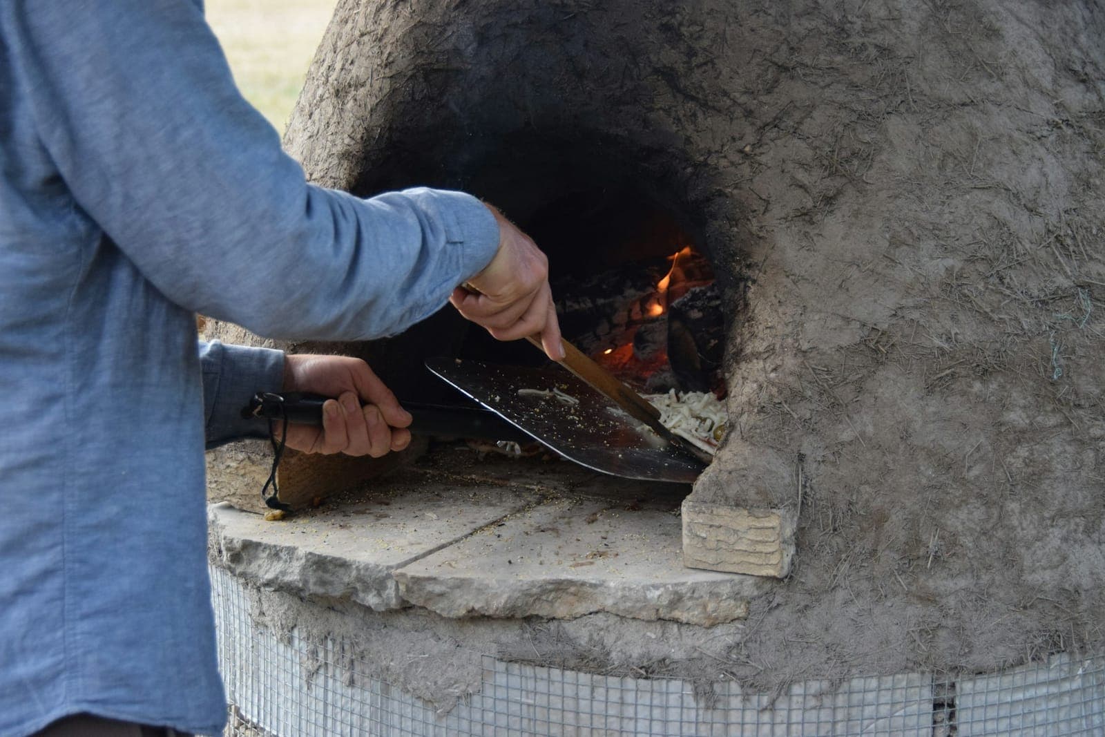Cook sliding a peel into an outdoor masonry pizza oven