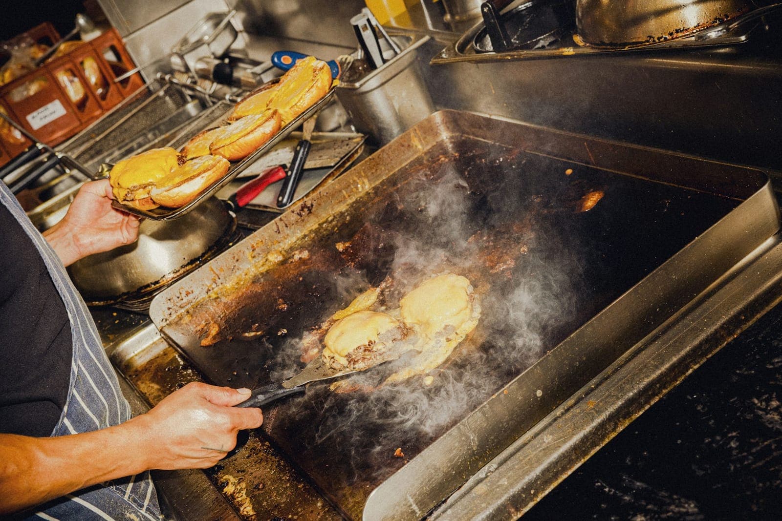 Cook working a hot flat-top griddle with a scraper