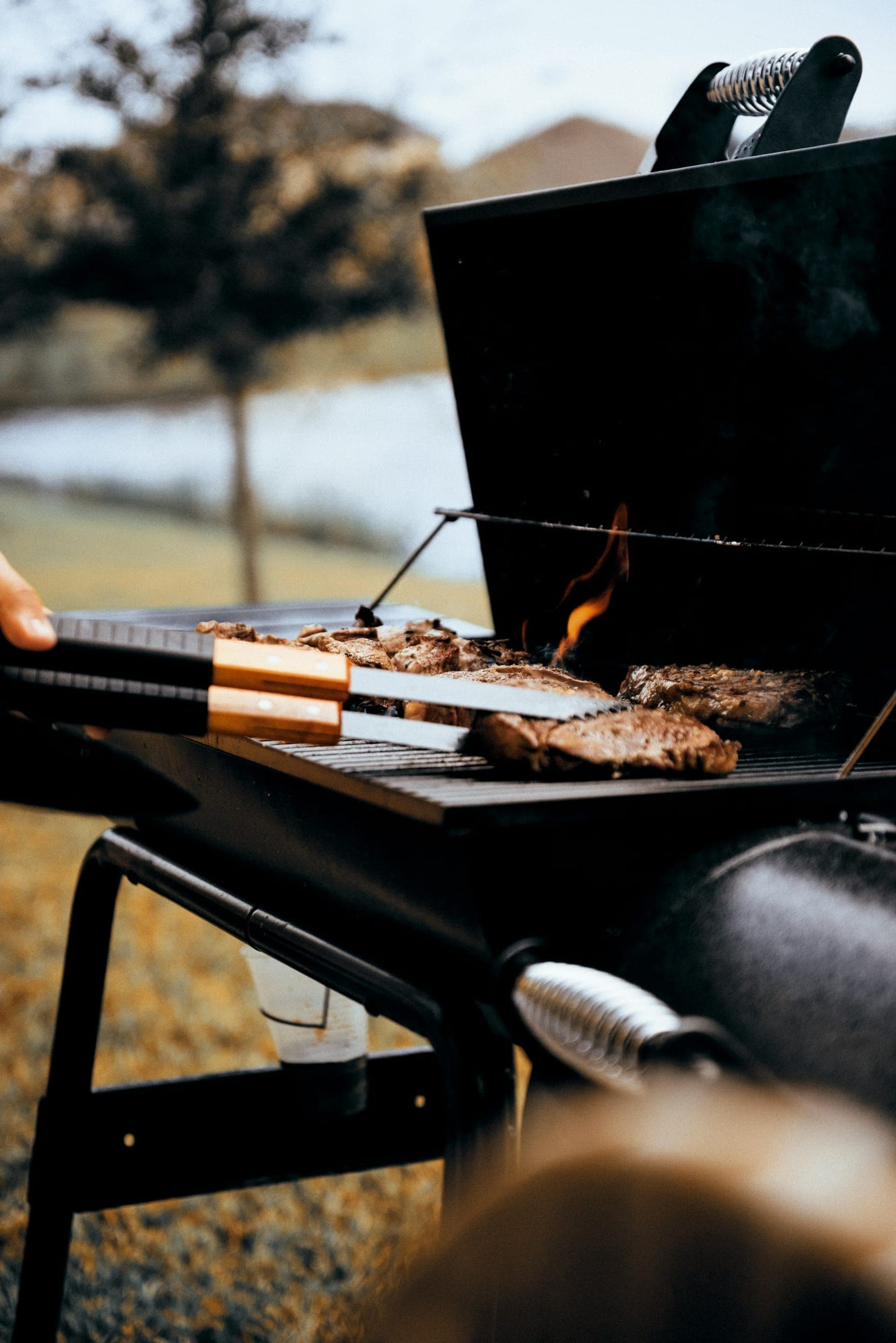 Tongs and spatula working food over a flaming grill