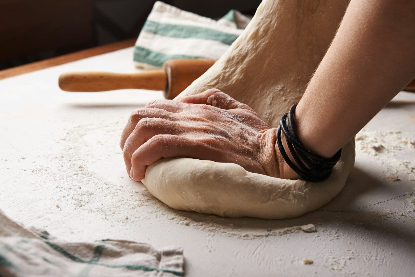 Hands kneading pizza dough on a floured counter